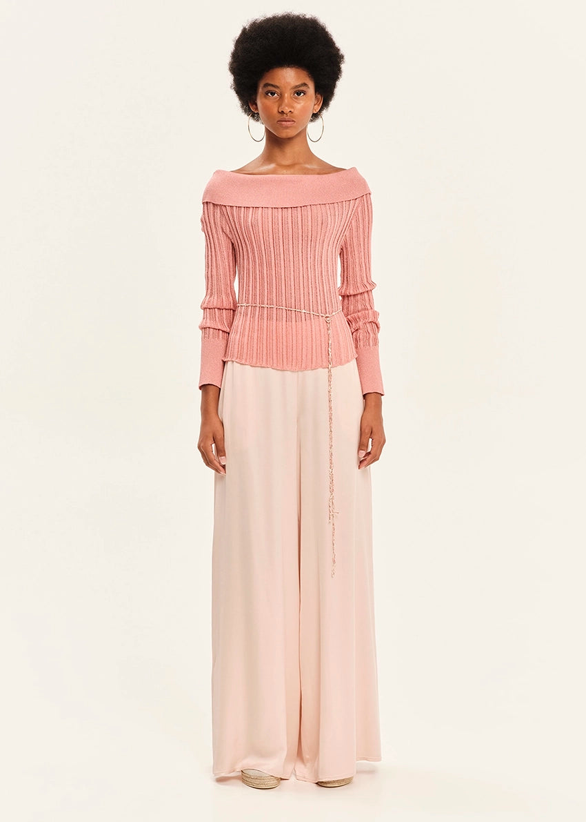 Woman wearing a pink ribbed top and light pink flowing pants on a white background