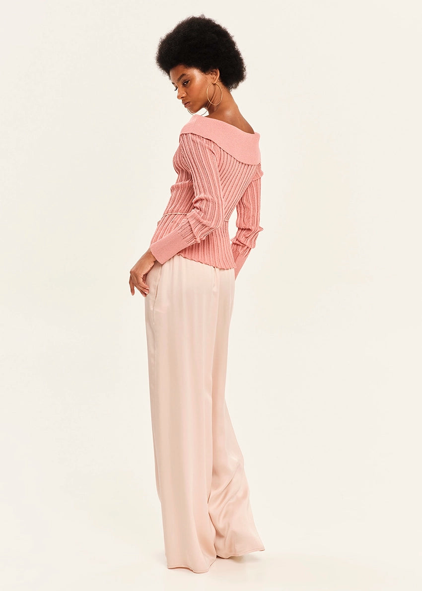 Woman wearing a pink blouse and pink pants on a light background