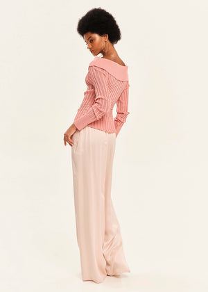 Woman wearing a pink blouse and pink pants on a light background
