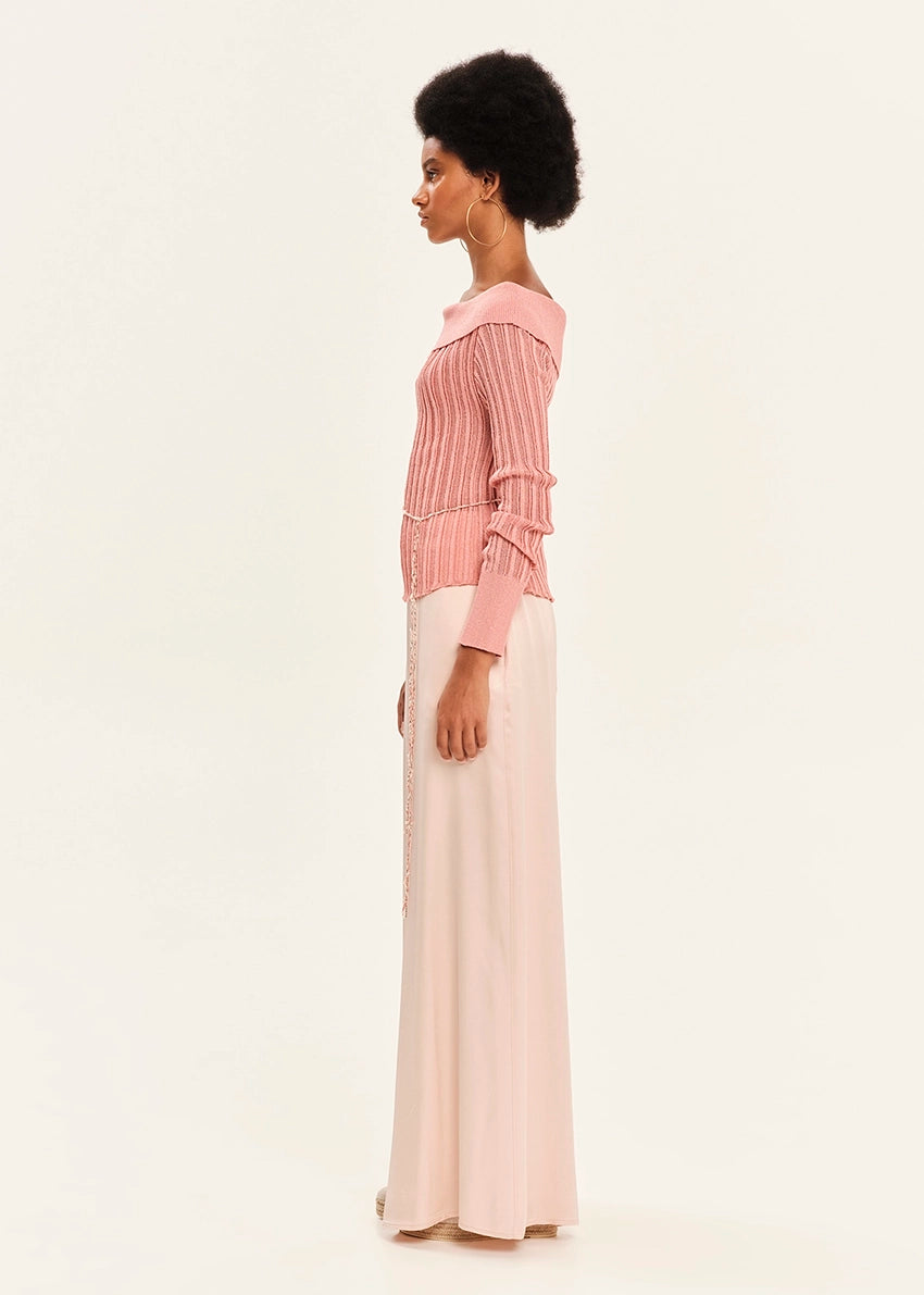 Woman wearing a pink blouse and white pants on a light background