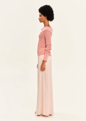 Woman wearing a pink blouse and white pants on a light background