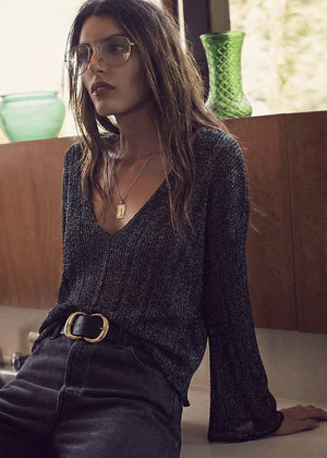 Woman wearing a dark ribbed sweater and glasses in a casual setting.