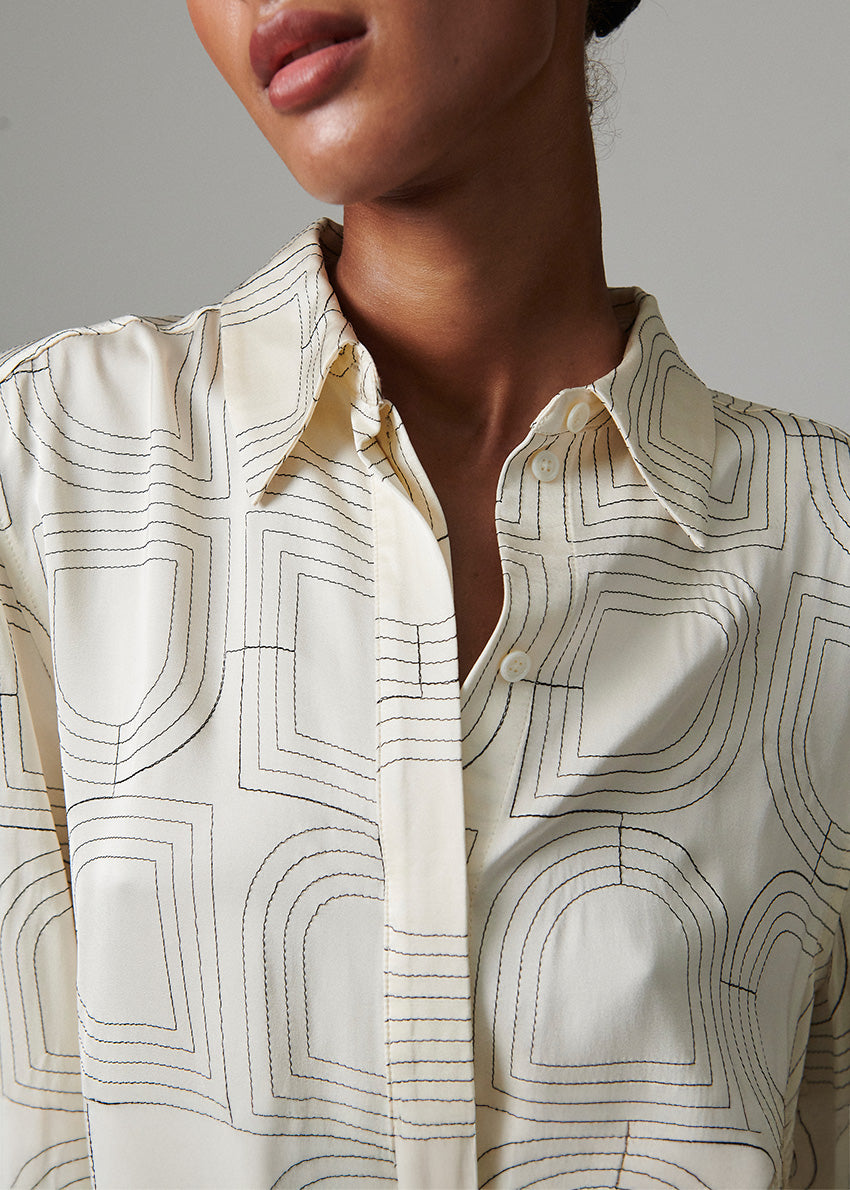 Close-up of a person wearing a white shirt with black geometric patterns on a neutral background