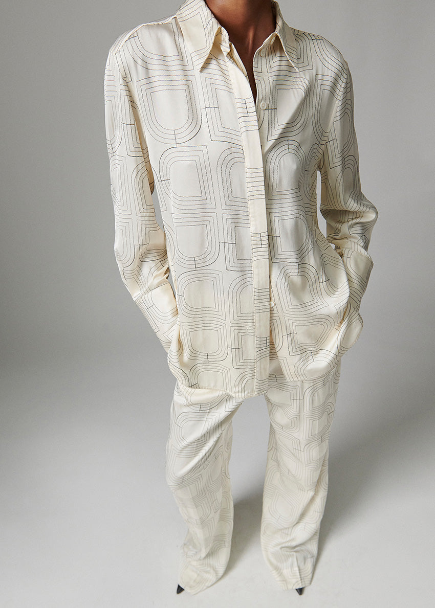 Person wearing a cream-colored patterned shirt and pants on a gray background
