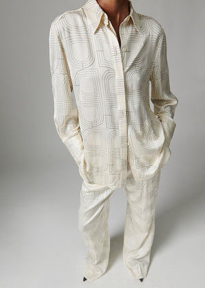 Person wearing a cream-colored patterned shirt and pants on a gray background