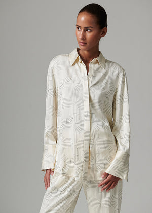Woman wearing a cream-colored patterned shirt and pants on a gray background
