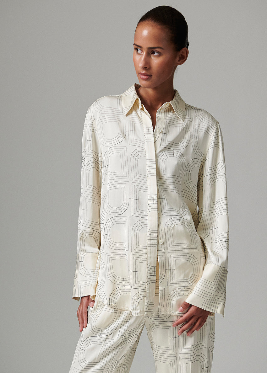 Woman wearing a cream-colored patterned shirt and pants on a gray background