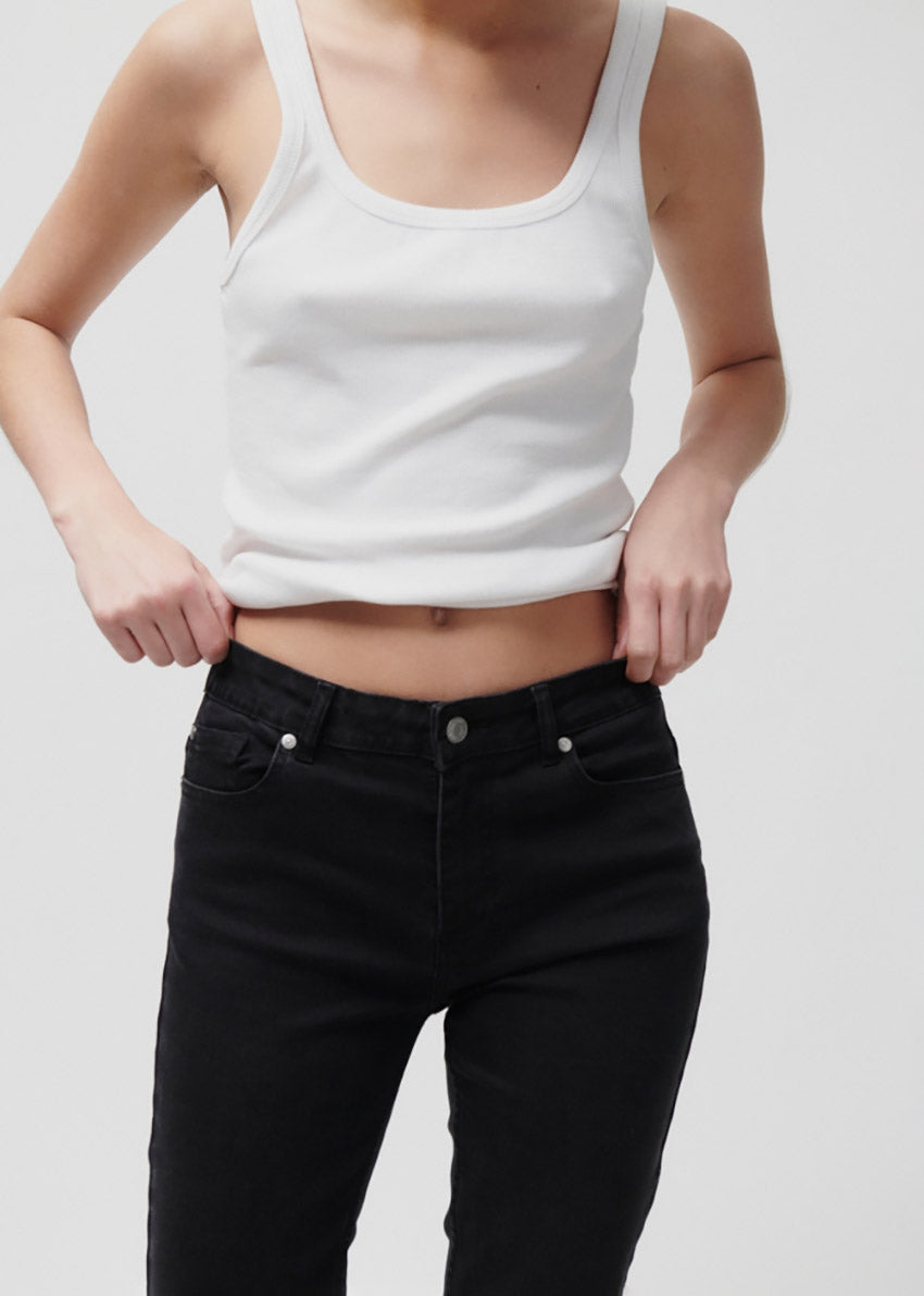 Person wearing a white tank top and black pants on a plain background