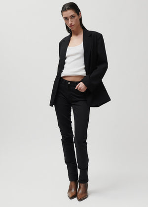 Person wearing a black blazer, white top, black pants, and brown boots on a light gray background