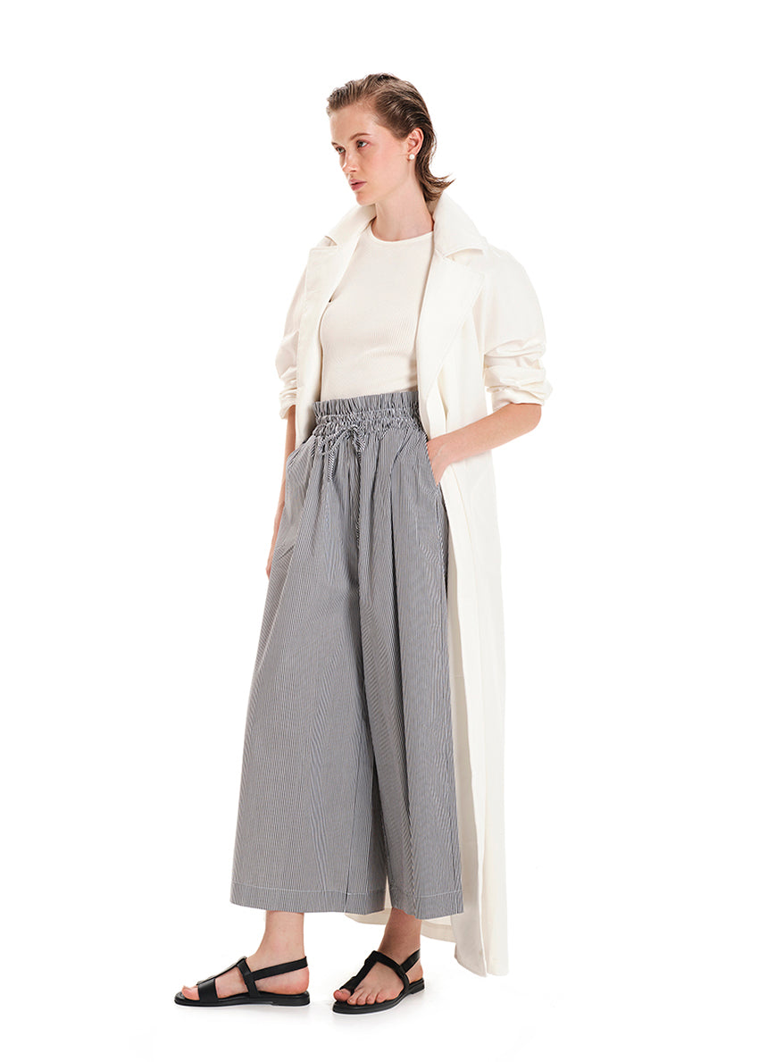 A model wearing wide leg striped pants with a rouched waist and a long beige top.