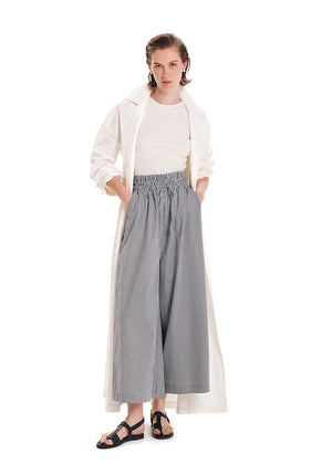 A model wearing wide leg striped pants with a rouched waist and a long beige top.