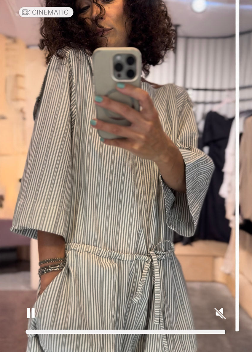 Person taking a mirror selfie wearing a striped dress in a store setting.