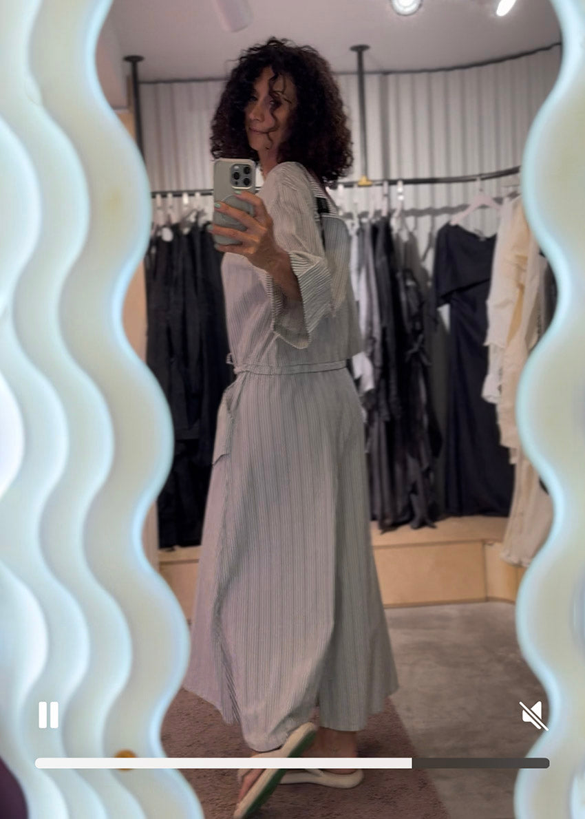 Woman taking a mirror selfie wearing a light gray dress in a clothing store.