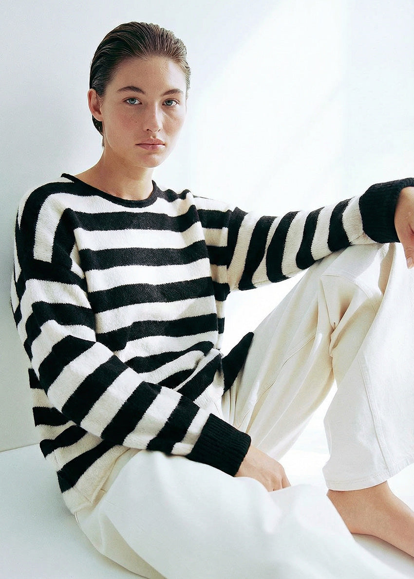 Person wearing a black and white striped sweater sitting on a white surface.