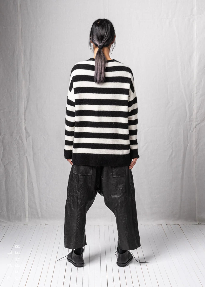 Person wearing a black and white striped sweater and dark pants against a plain background