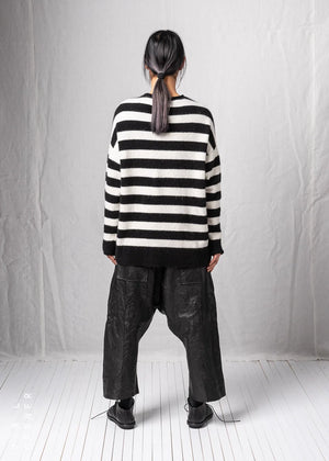 Person wearing a black and white striped sweater and dark pants against a plain background