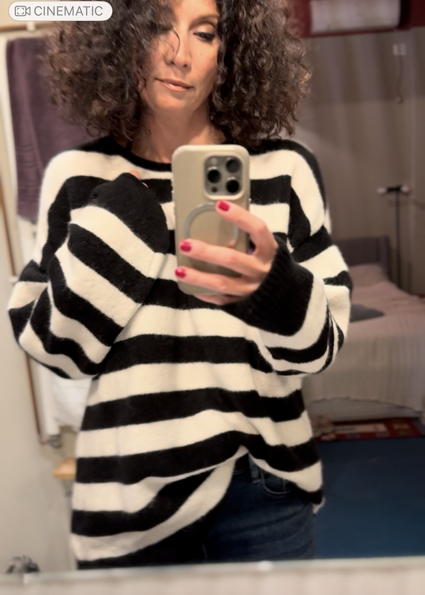 Woman wearing a black and white striped sweater taking a mirror selfie.