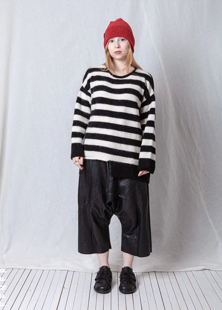 Person wearing a black and white striped sweater and black leather pants against a plain background