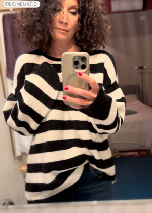 Woman wearing a black and white striped sweater taking a mirror selfie.