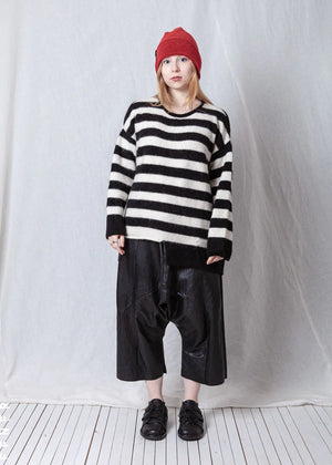 Person wearing a black and white striped sweater and black leather pants against a plain background