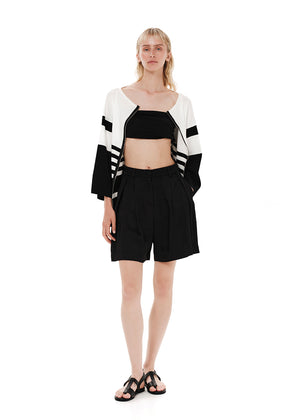 A striped cardigan with color block design in white and black, featuring a front zipper closure and bell sleeves.