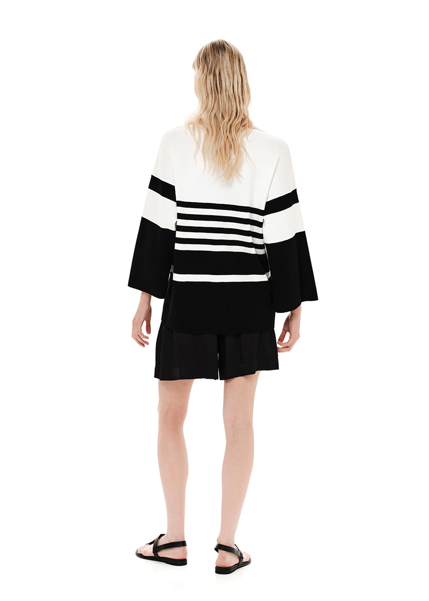 A striped cardigan with color block design in white and black, featuring a front zipper closure and bell sleeves.