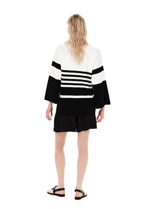 A striped cardigan with color block design in white and black, featuring a front zipper closure and bell sleeves.