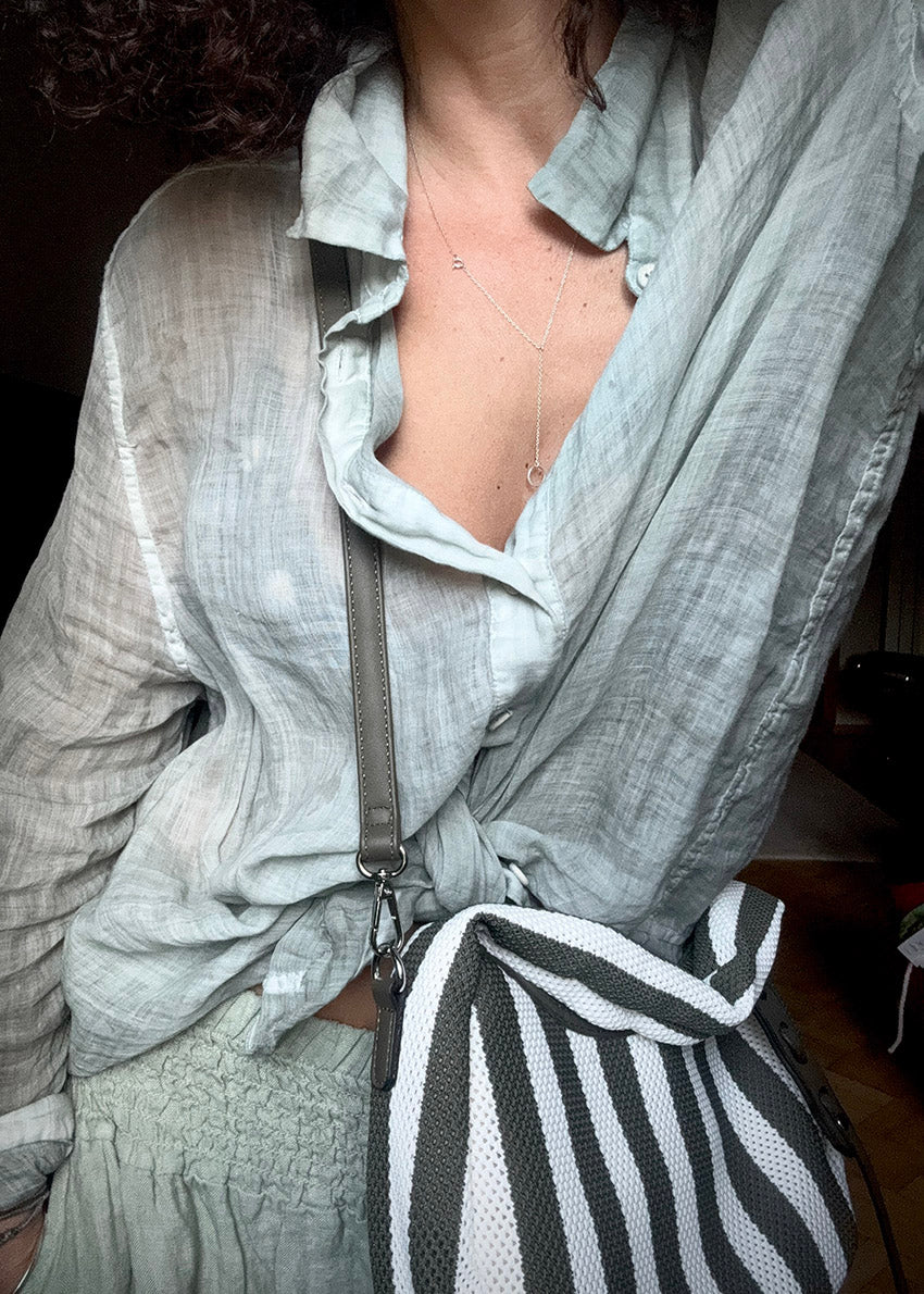 Person wearing a light gray shirt with a khaki and white striped bag over their shoulder.