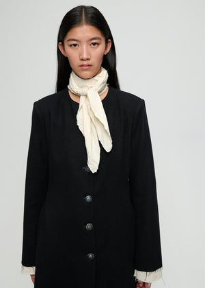 Person wearing a black coat with a white scarf on a plain background