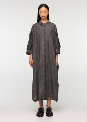 A person standing wearing a long, loose-fitting, grey shirt with 3/4-length sleeves, a collar, and buttons down the front. The shirt features a decorative vertical belt at the back and two side pockets.