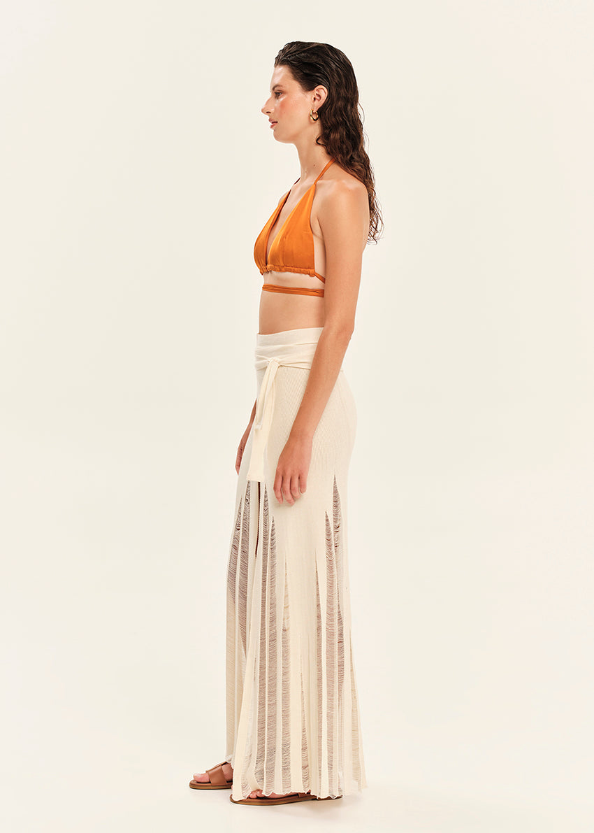 Woman wearing a mustard yellow top and beige skirt on a white background