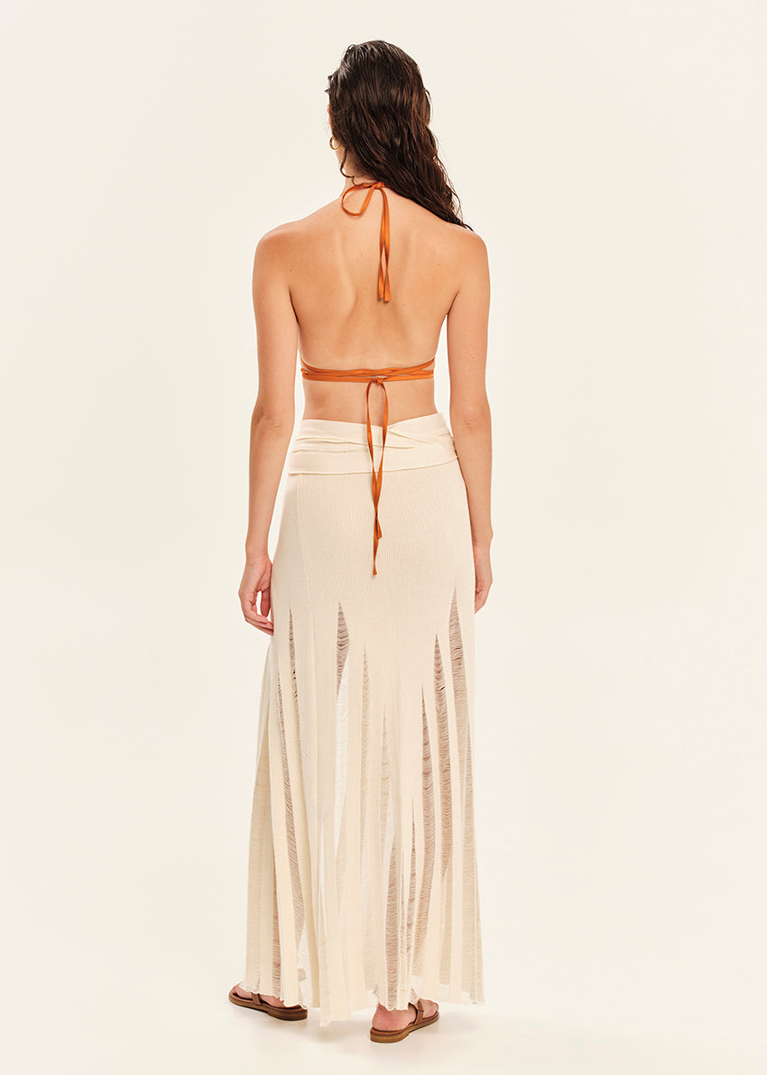 Woman wearing an orange halter top and white skirt with a slit on a beige background