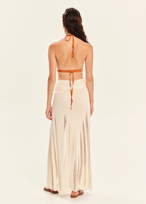 Woman wearing an orange halter top and white skirt with a slit on a beige background