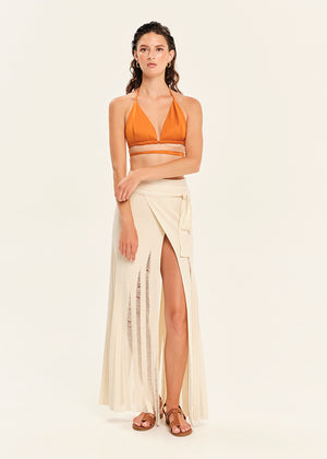 Woman wearing a mustard yellow bikini top and white skirt on a beige background