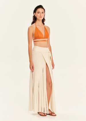 Woman wearing an orange halter top and white skirt with a slit on a beige background