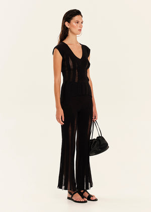 Woman wearing a black sleeveless top with matching pants holding a black handbag on a white background