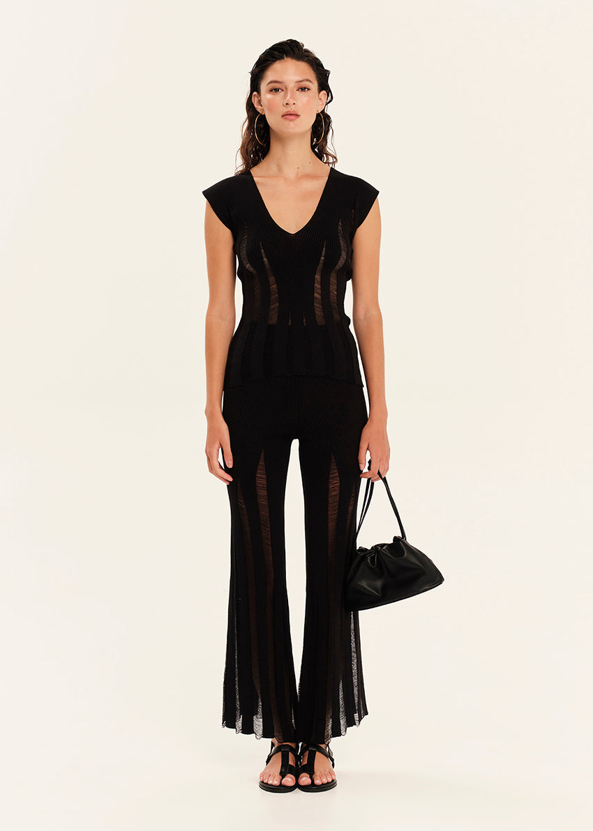 Woman wearing a black sleeveless top and black pants with sheer panels on a white background