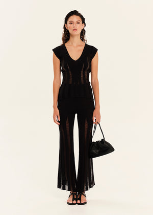 Woman wearing a black sleeveless top and black pants with sheer panels on a white background