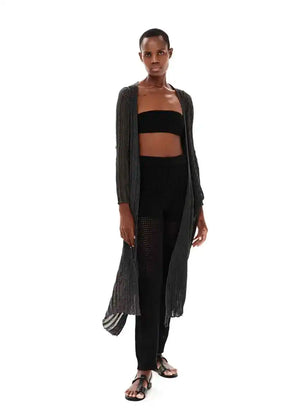 A model wearing a long black cardigan over a black top and matching pants, standing against a white background.