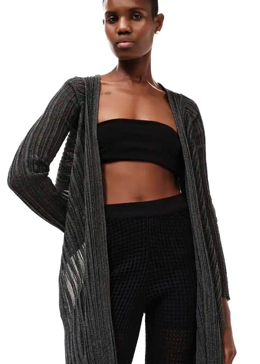 A model wearing a long black cardigan over a black top and matching pants, standing against a white background.