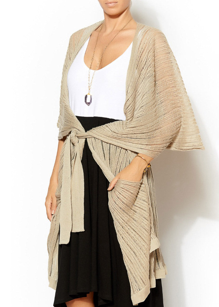 Woman wearing a beige cardigan over a white top and black skirt on a white background