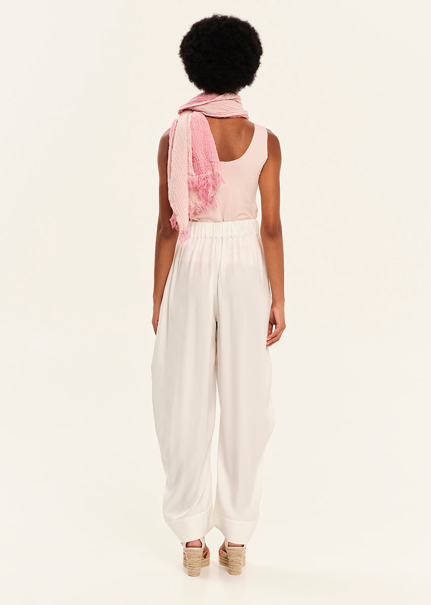 Person wearing a pink top and white pants with a scarf over shoulders on a light background