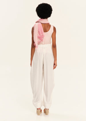 Person wearing a pink top and white pants with a scarf over shoulders on a light background