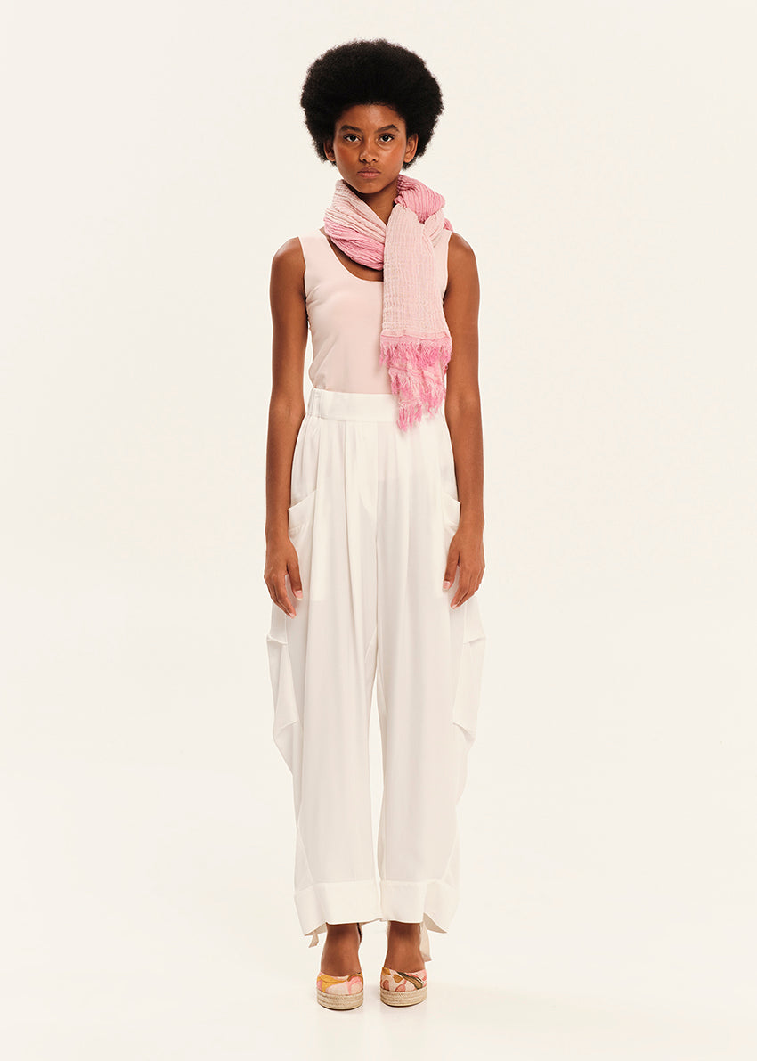 Woman wearing a pink scarf and pink tank top with white pants on a white background