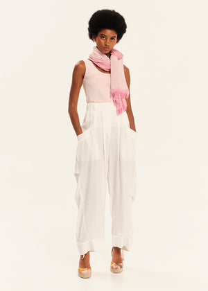Woman wearing a pink top and white pants with a pink scarf on a white background