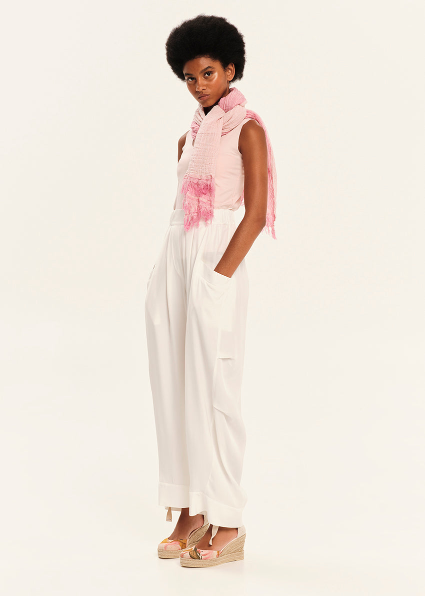 Woman wearing a pink sleeveless top and white pants on a white background