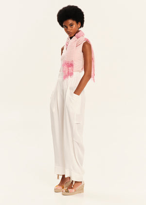 Woman wearing a pink sleeveless top and white pants on a white background