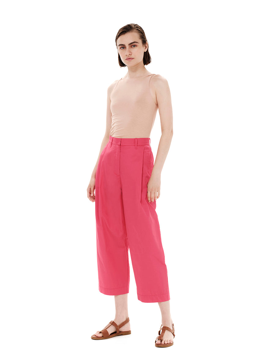 Person wearing a beige tank top with pink trousers on a white background 