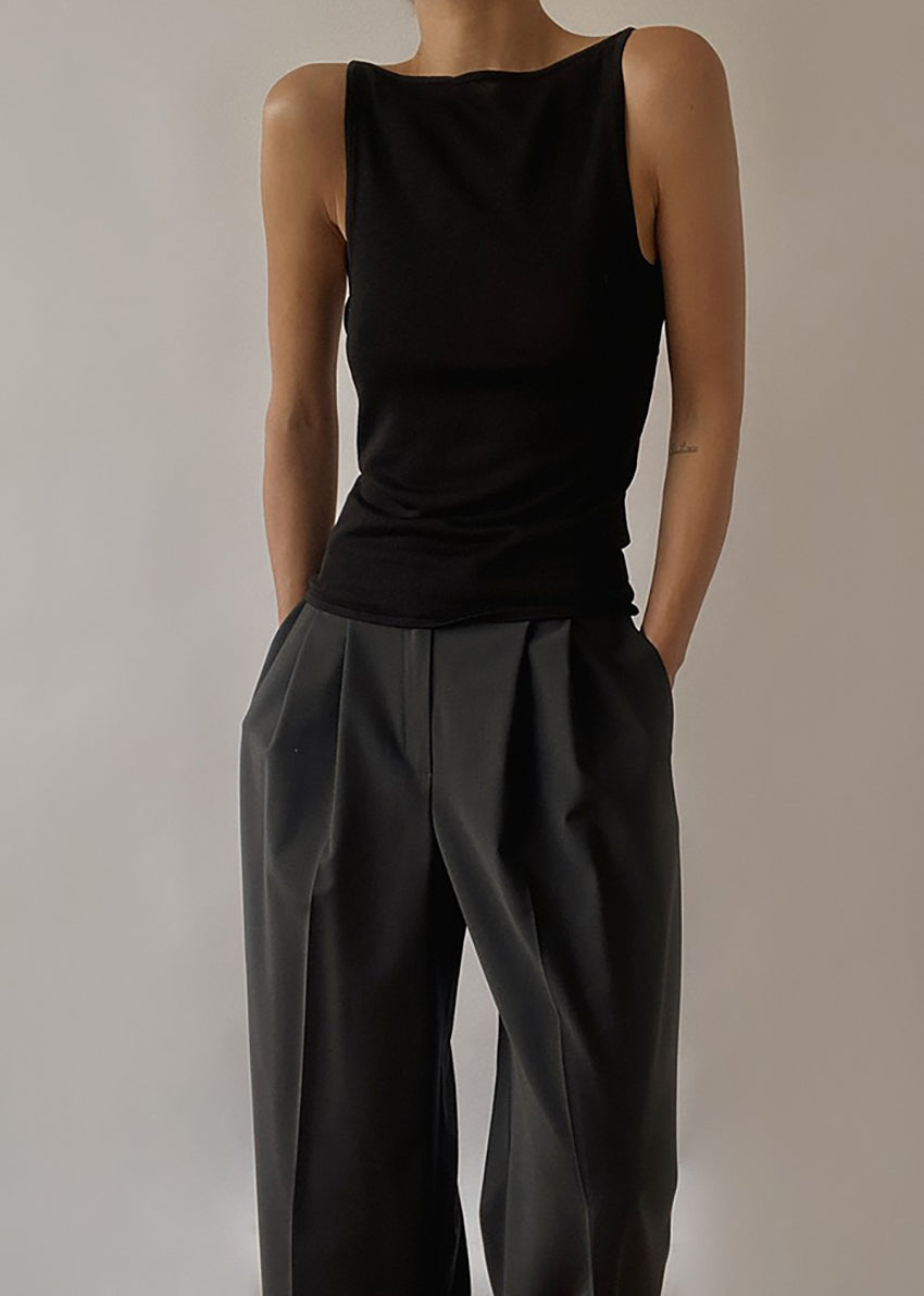 A person wearing a black sleeveless tank top with a V-shaped back and matching grey trousers.