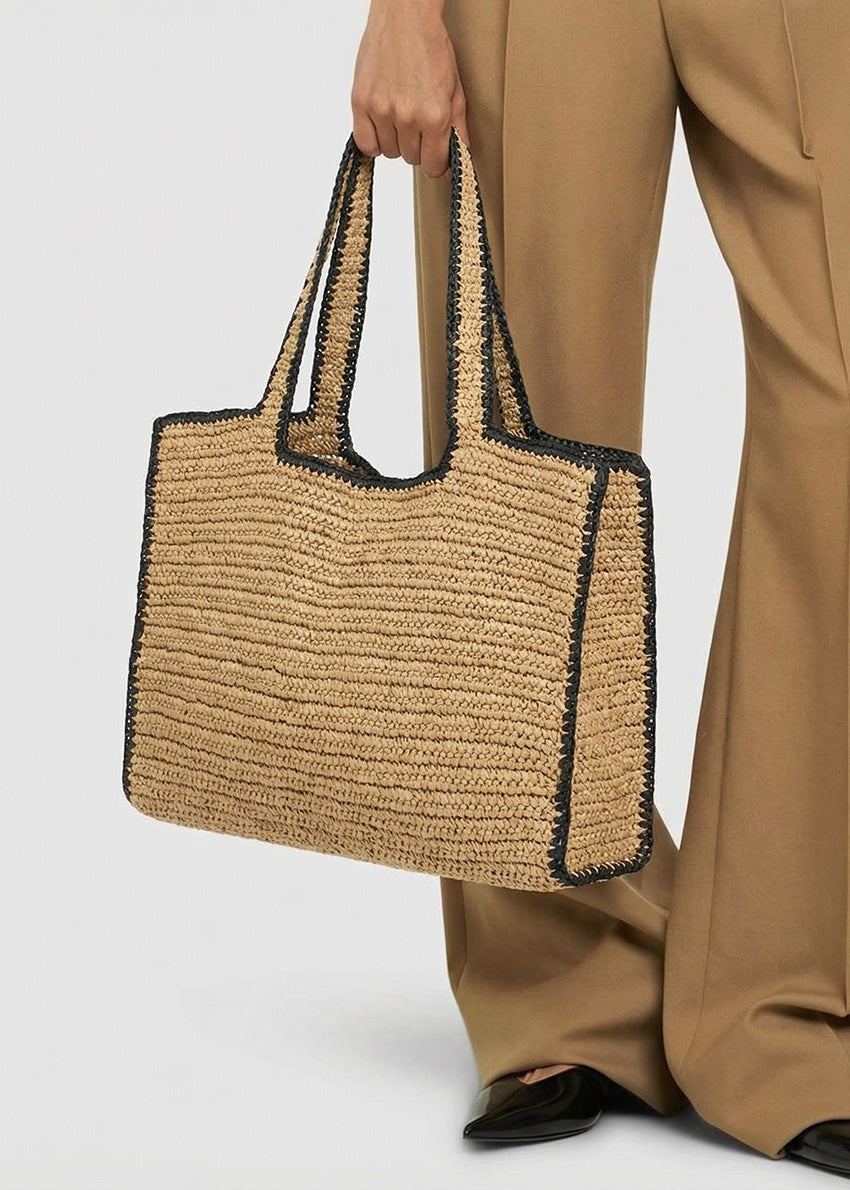 Person holding a woven handbag with black accents on a plain background